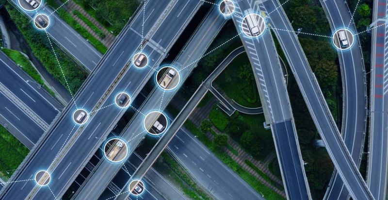 Aerial view of connected vehicles on layered highway overpasses, representing networked autonomy and road safety